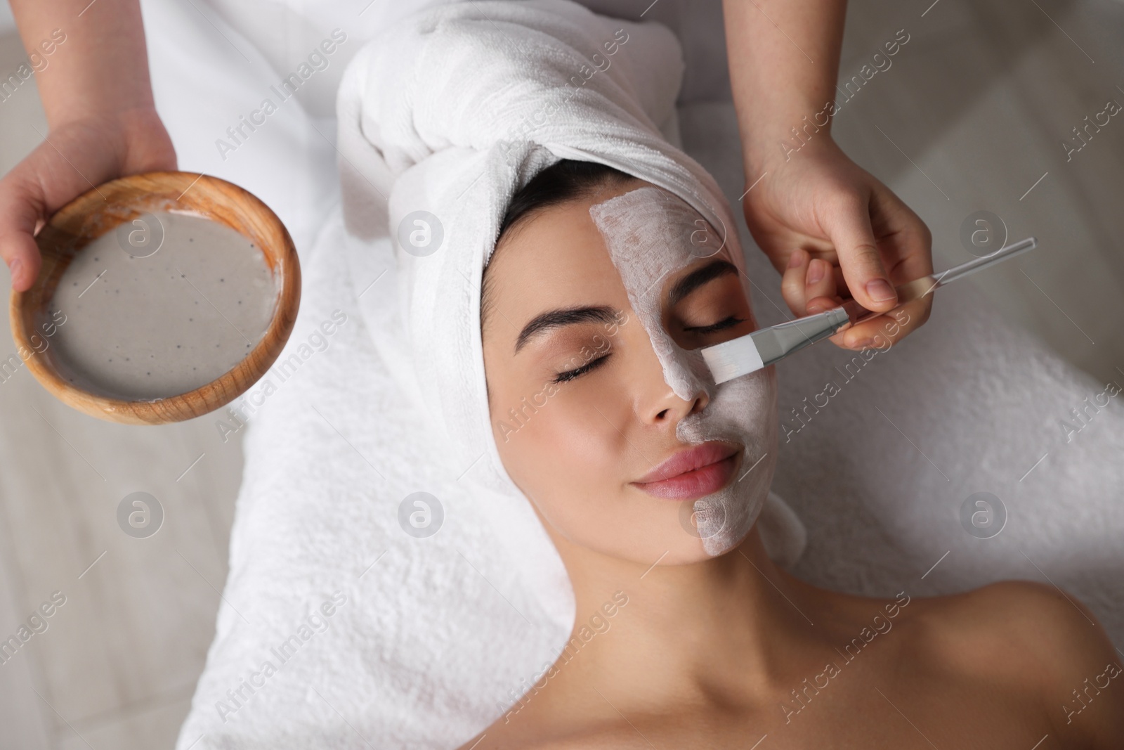 Photo of Cosmetologist applying mask on woman's face in spa salon, above view