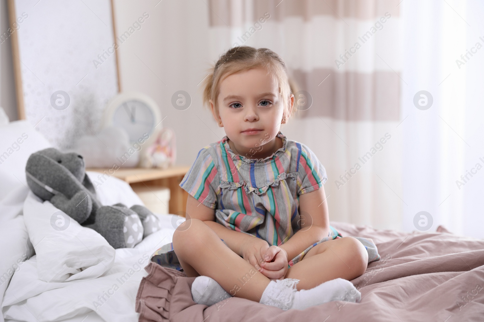 Photo of Cute little girl sitting on bed at home