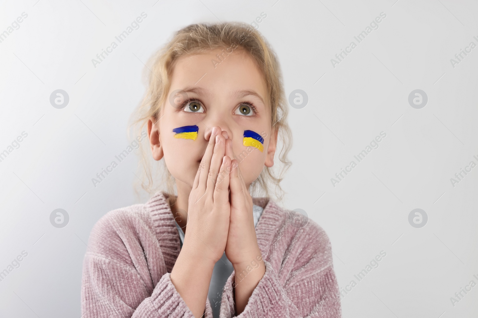 Photo of Little girl with drawings of Ukrainian flag on face and clasped hands against white background