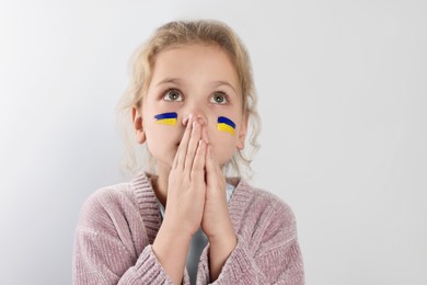 Photo of Little girl with drawings of Ukrainian flag on face and clasped hands against white background