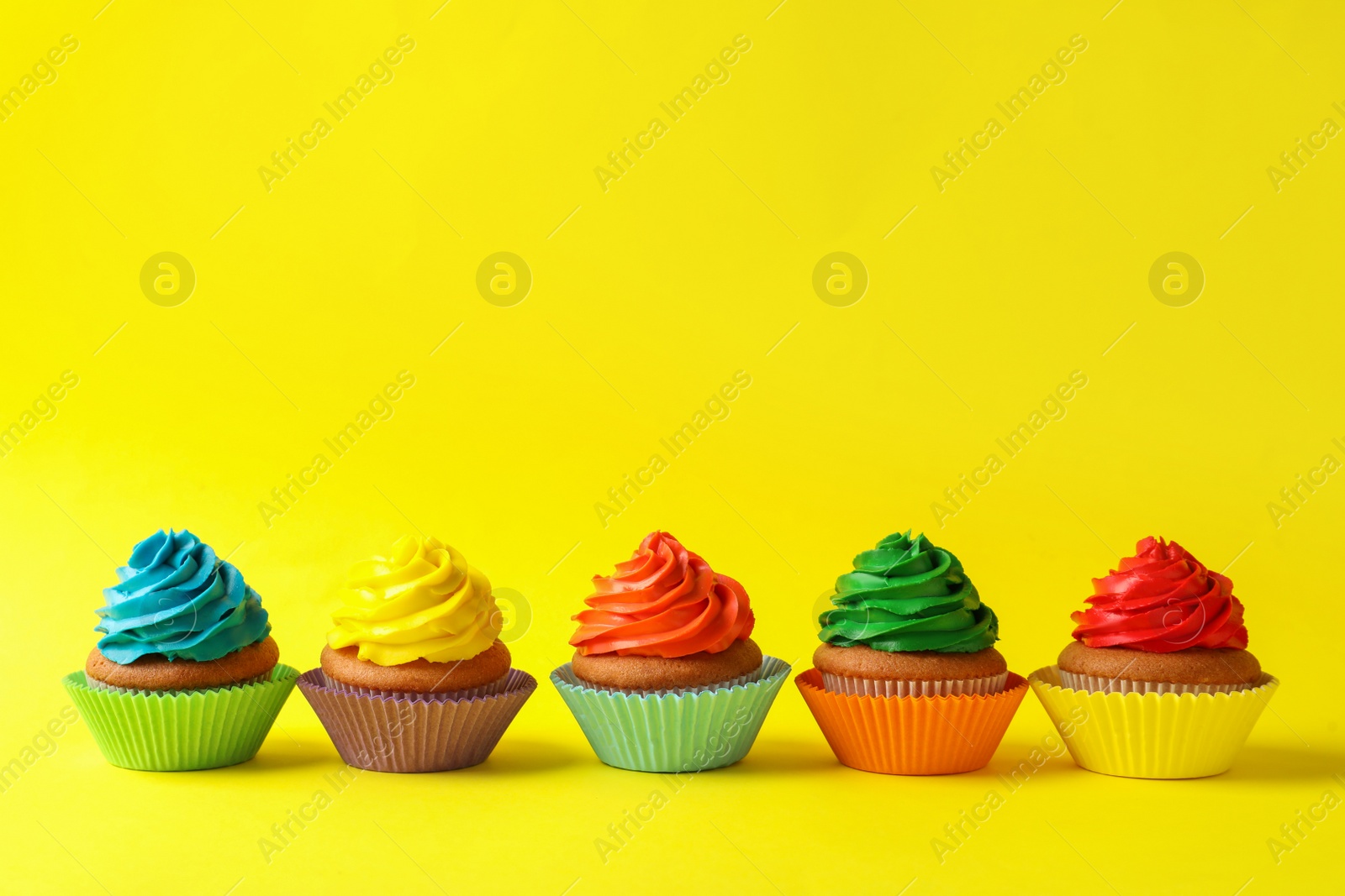 Photo of Delicious colorful cupcakes on yellow background. Space for text