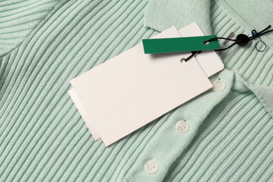 Photo of Blank white tags on mint knitted shirt, top view. Space for text