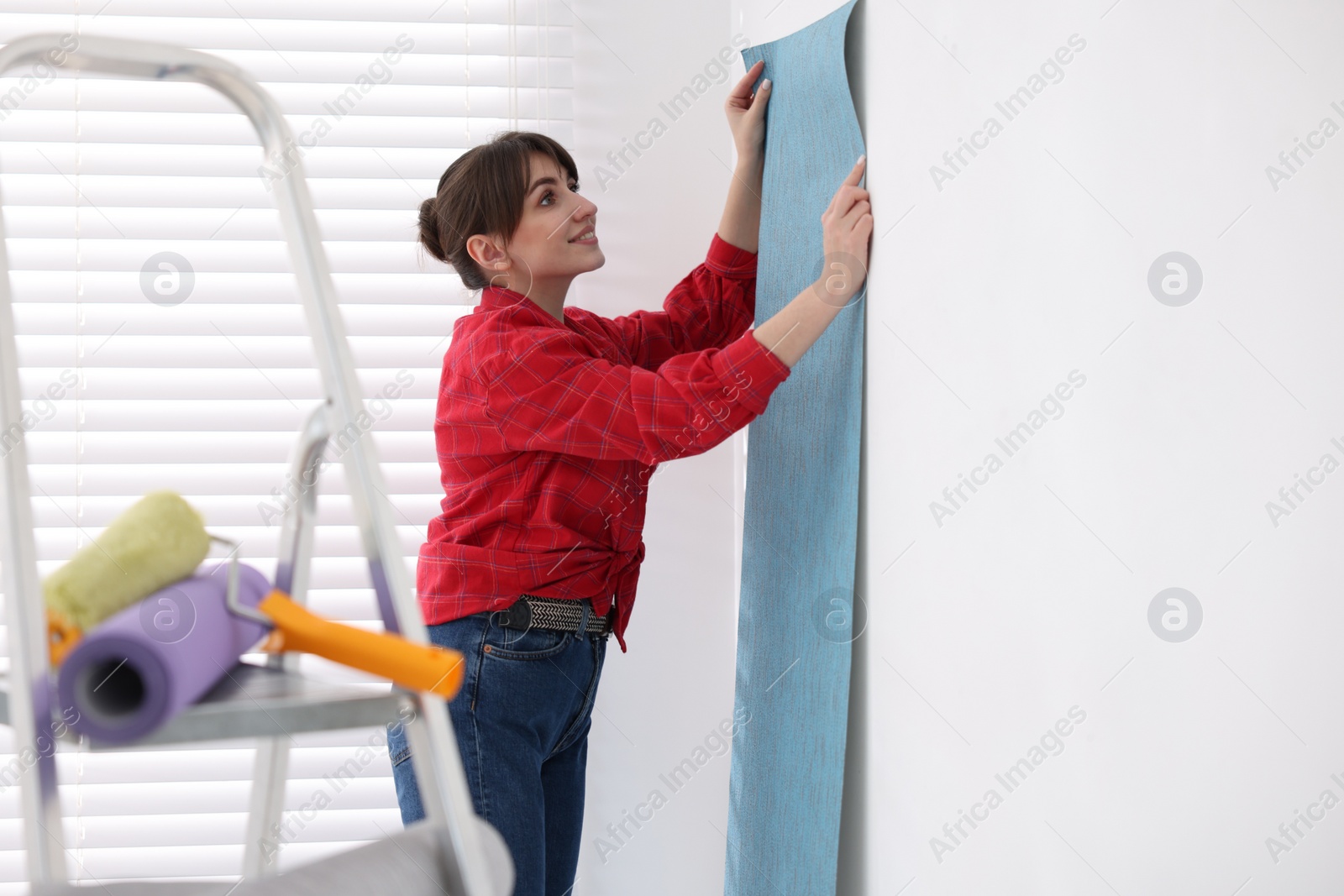 Photo of Woman hanging light blue wallpaper in room