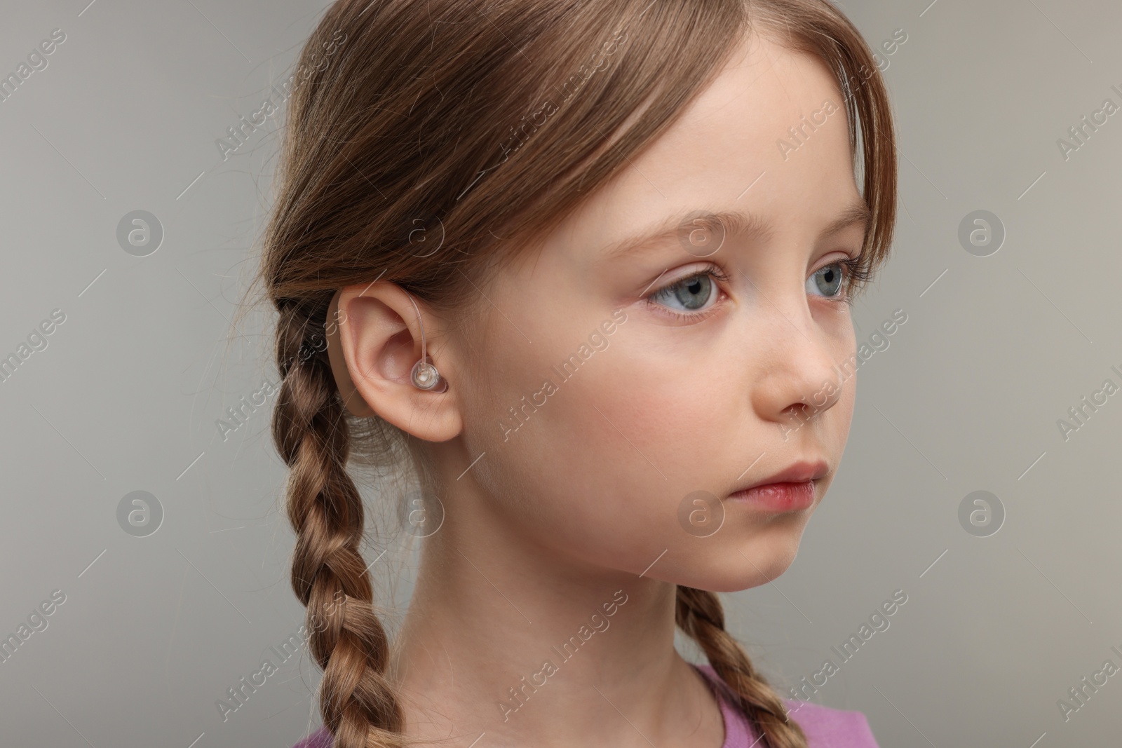 Photo of Little girl with hearing aid on grey background, closeup