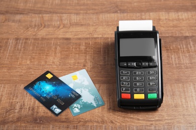 Photo of Modern payment terminal and credit cards on wooden background. Space for text