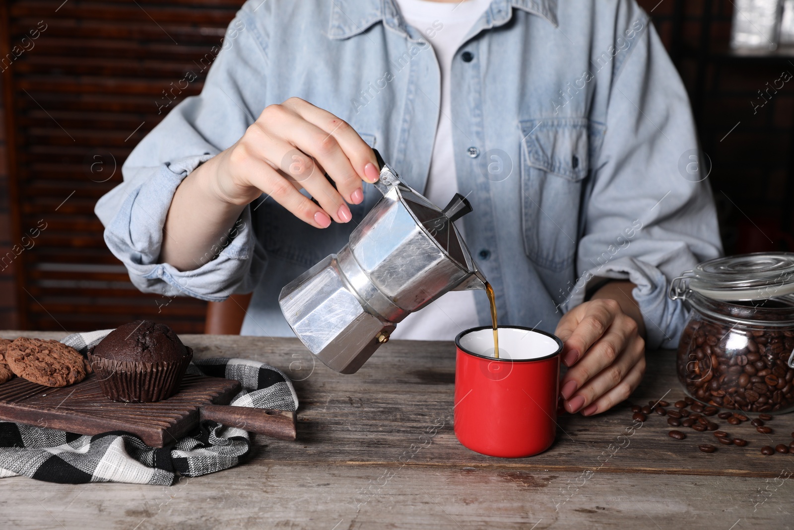 Photo of Woman pouring aromatic coffee from moka pot into cup at wooden table indoors, closeup