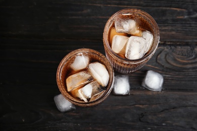 Glasses of refreshing cola with ice cubes on wooden background, top view