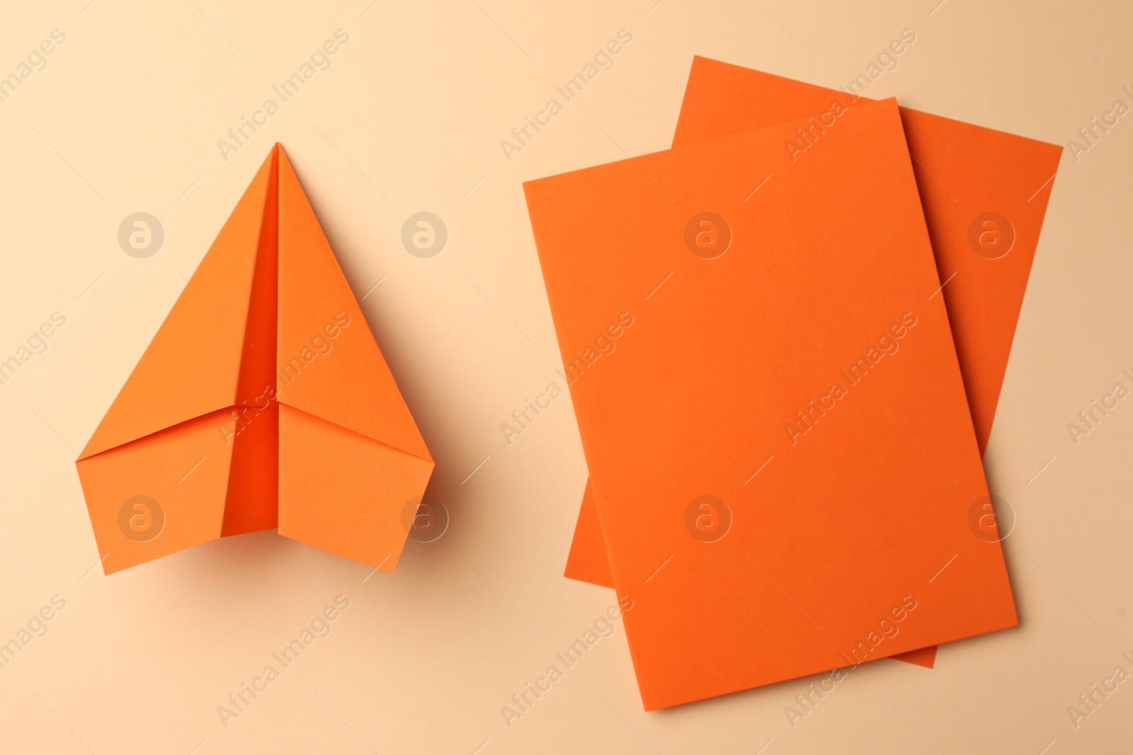 Photo of Handmade orange plane and pieces of paper on beige background, flat lay