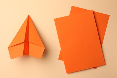 Handmade orange plane and pieces of paper on beige background, flat lay