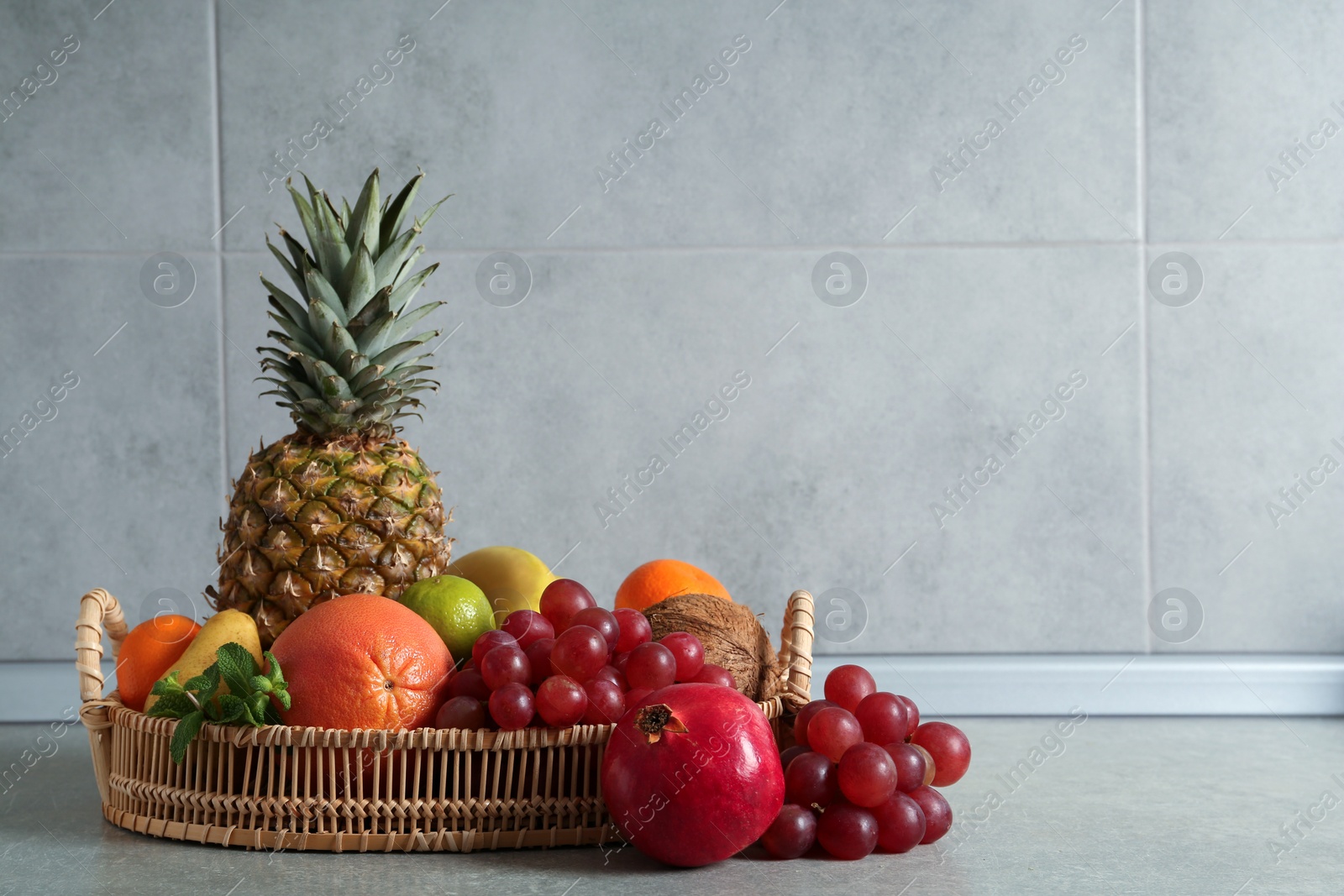 Photo of Wicker tray and different ripe fruits on grey table. Space for text