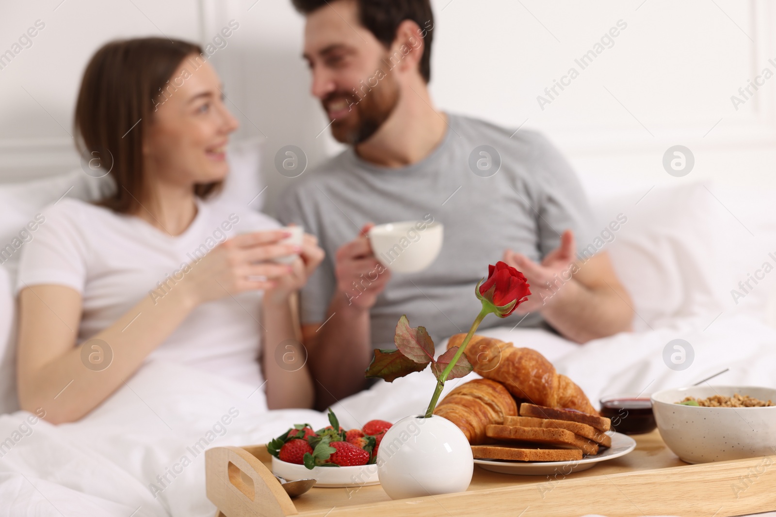 Photo of Tray with tasty breakfast in bed. Happy couple drinking coffee, selective focus