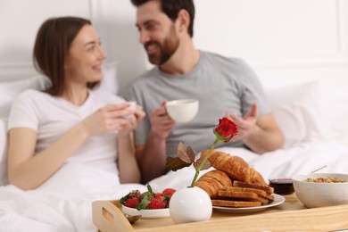 Photo of Tray with tasty breakfast in bed. Happy couple drinking coffee, selective focus