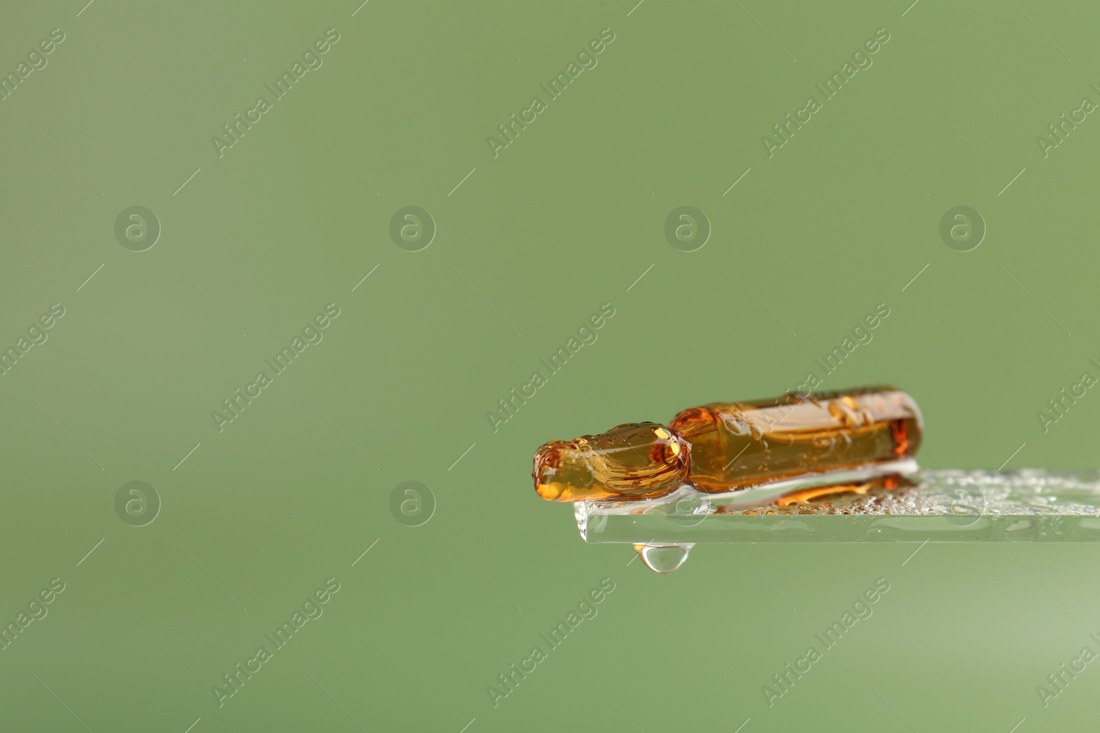 Photo of Wet skincare ampoule on light green background, closeup. Space for text