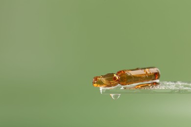 Wet skincare ampoule on light green background, closeup. Space for text