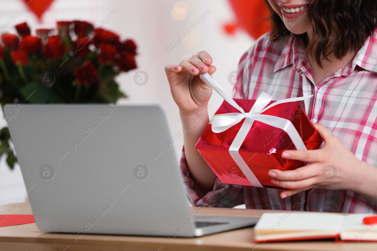 Photo of Valentine's day celebration in long distance relationship. Woman opening gift from her boyfriend indoors, closeup