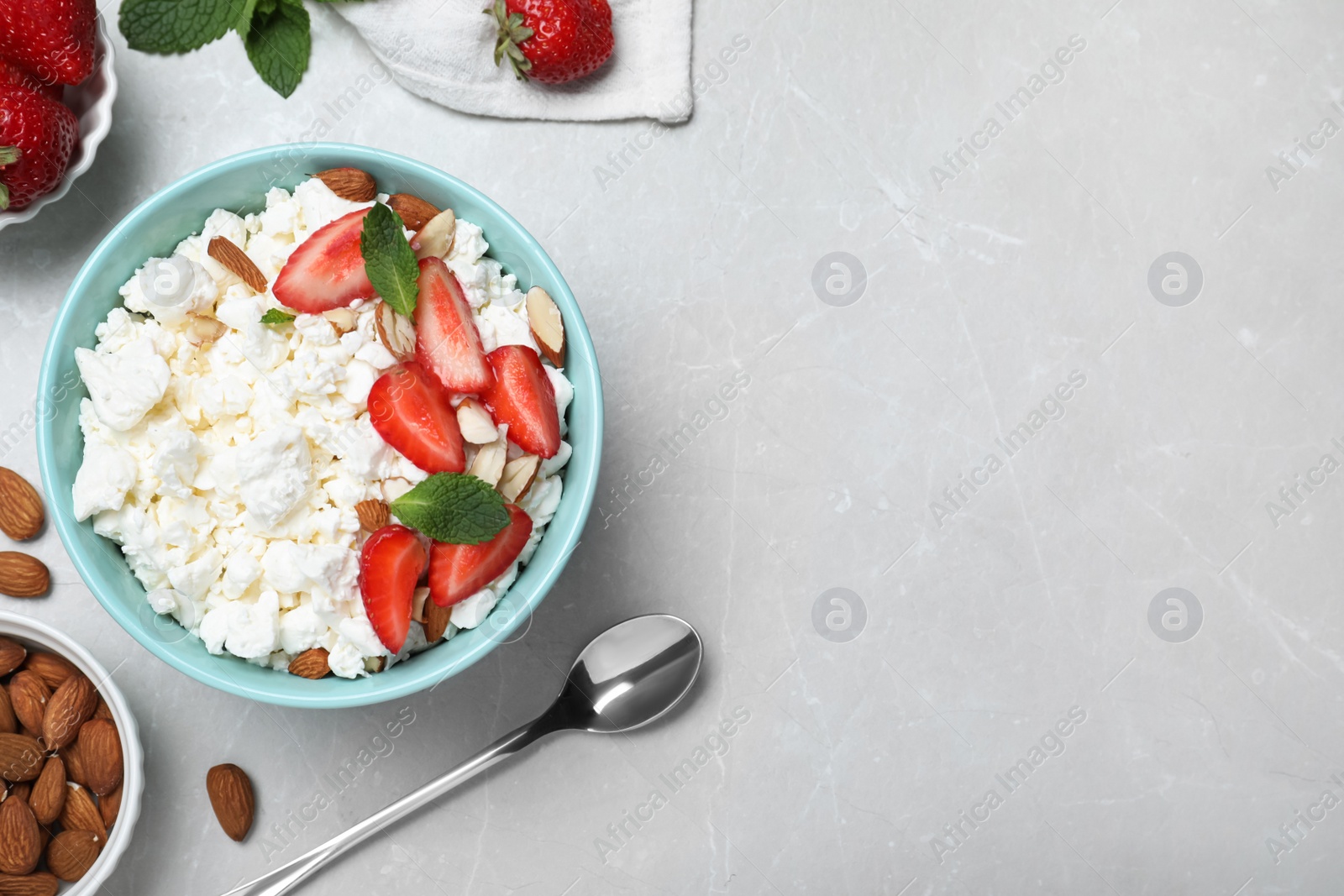 Photo of Fresh cottage cheese with strawberry and almond in bowl on light marble table, flat lay. Space for text