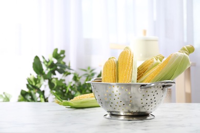 Photo of Colander with tasty sweet corn cobs on table