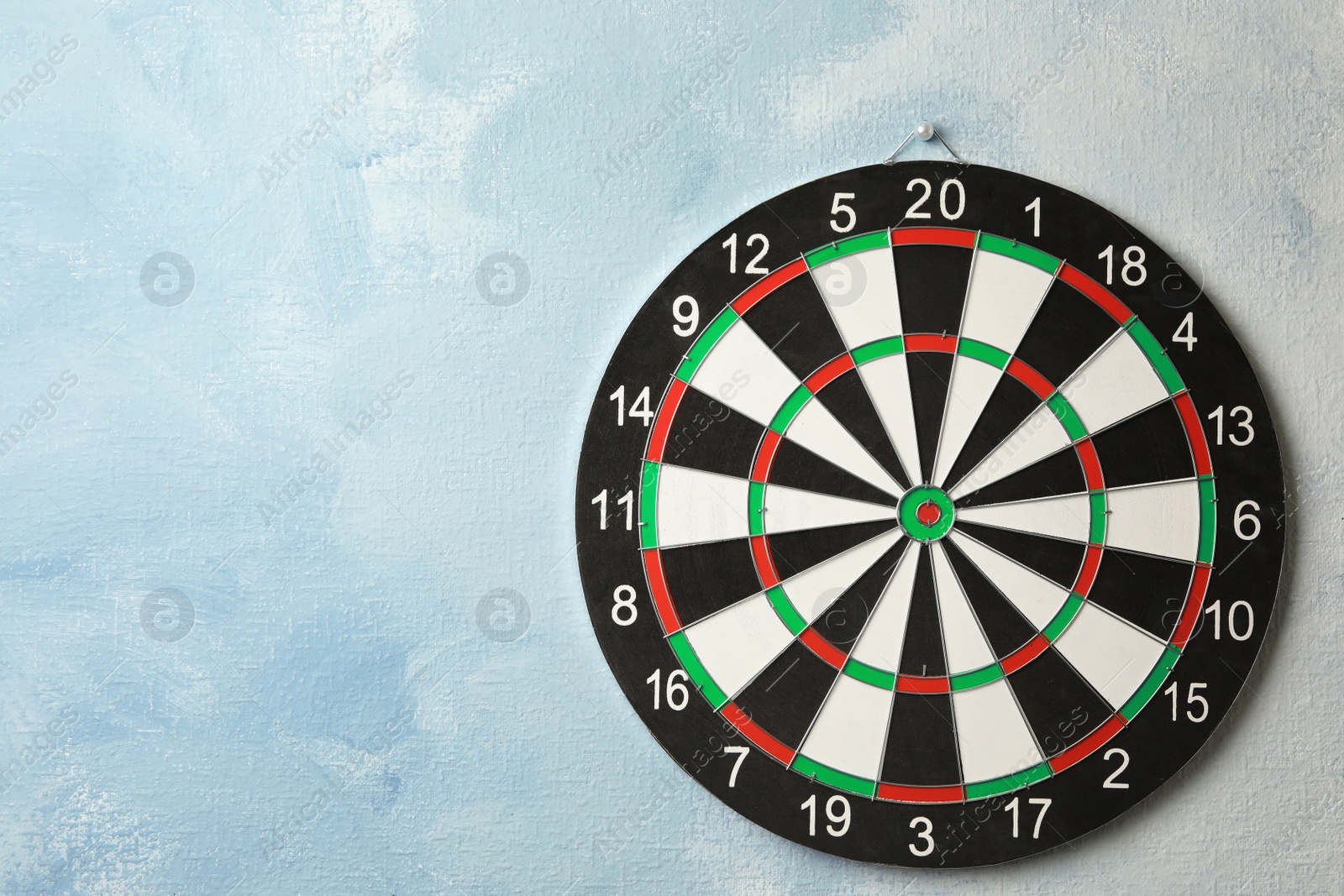 Photo of Dart board hanging on light blue wall. Space for text