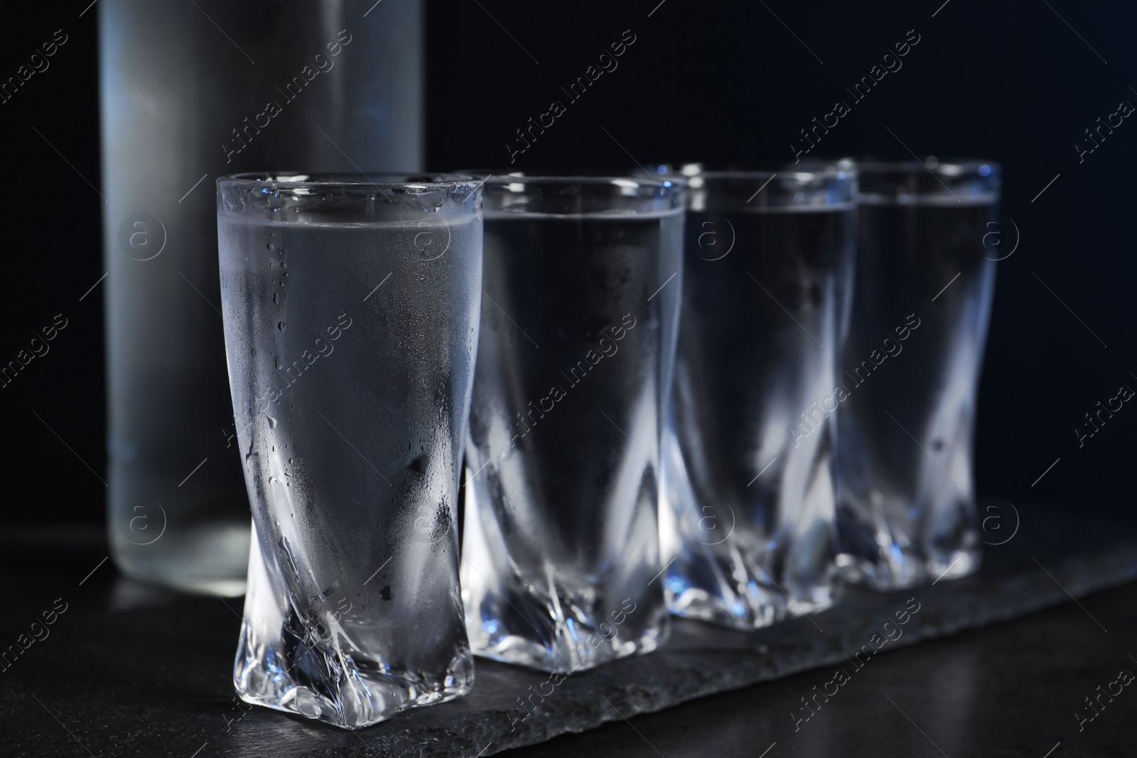 Photo of Set of glasses with vodka on black table, closeup