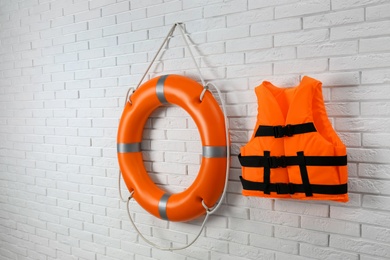 Photo of Orange life jacket and lifebuoy on white brick wall. Rescue equipment