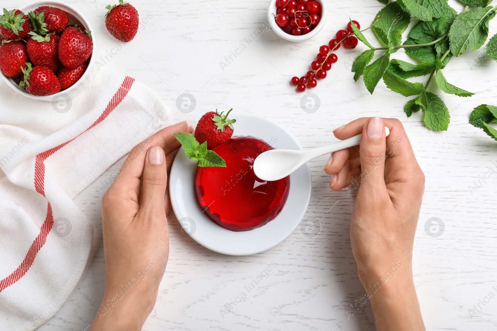 Photo of Woman eating delicious fresh red jelly at white wooden table, top view