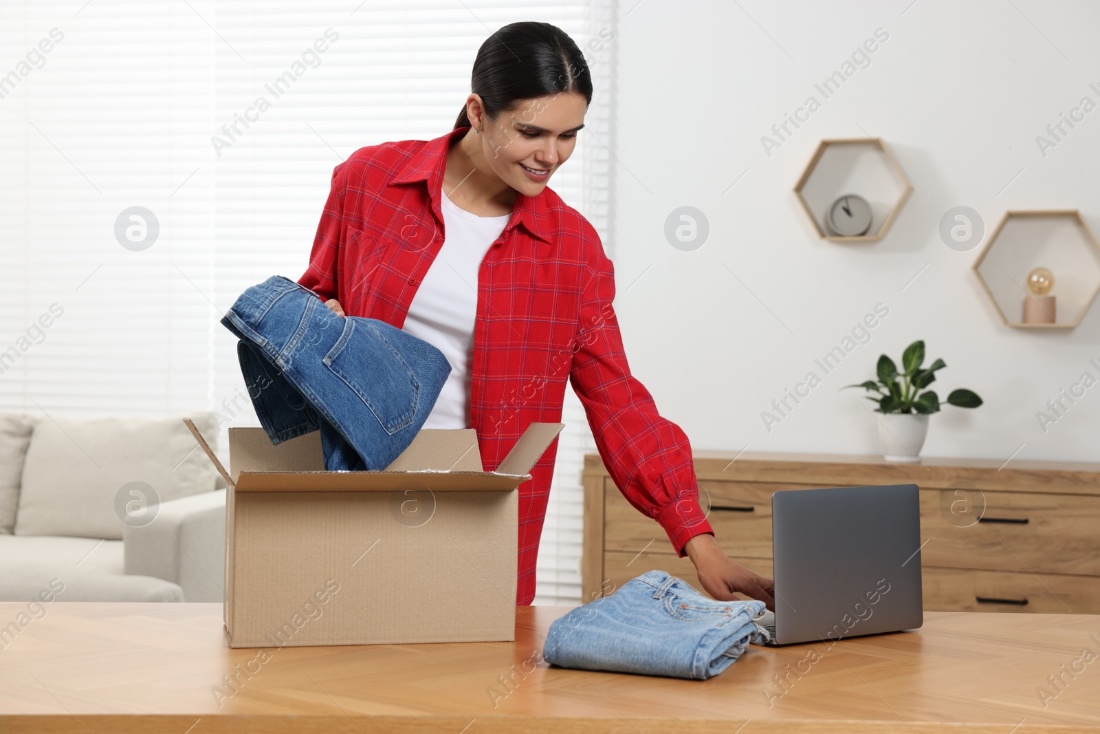 Photo of Young with just unpacked new jeans using laptop at table indoors. Online shopping