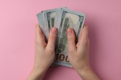 Photo of Money exchange. Woman holding dollar banknotes on pink background, top view