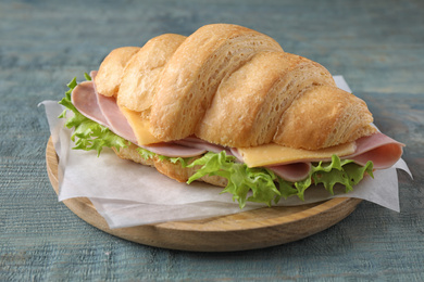Photo of Tasty croissant sandwich with ham on light blue wooden table