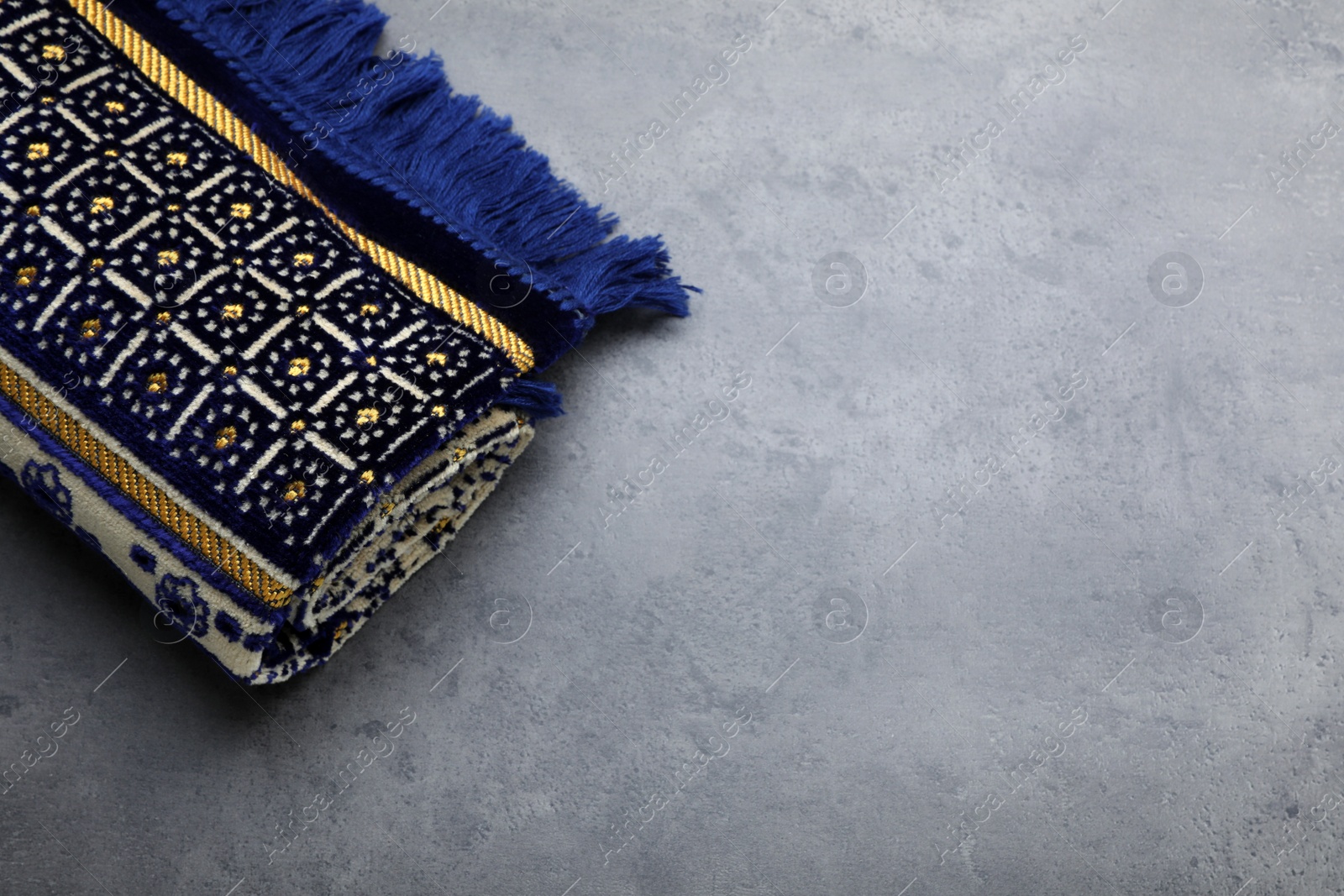 Photo of Muslim prayer rug on grey stone table, above view. Space for text