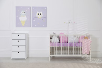 Photo of Crib and dresser near wall with pictures in cozy baby room. Interior design