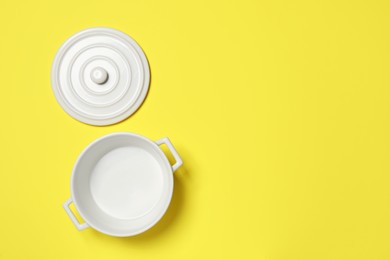 Photo of White empty pot and lid on yellow background, flat lay. Space for text