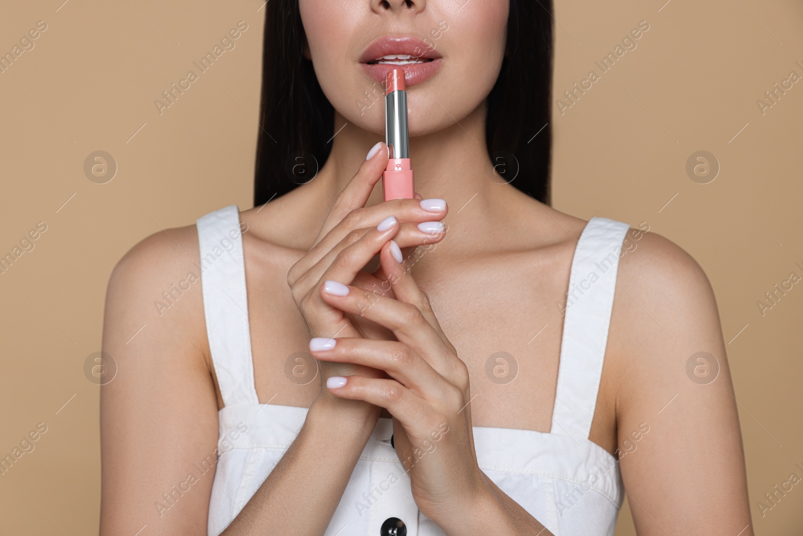 Photo of Young woman with beautiful makeup holding nude lipstick on beige background, closeup