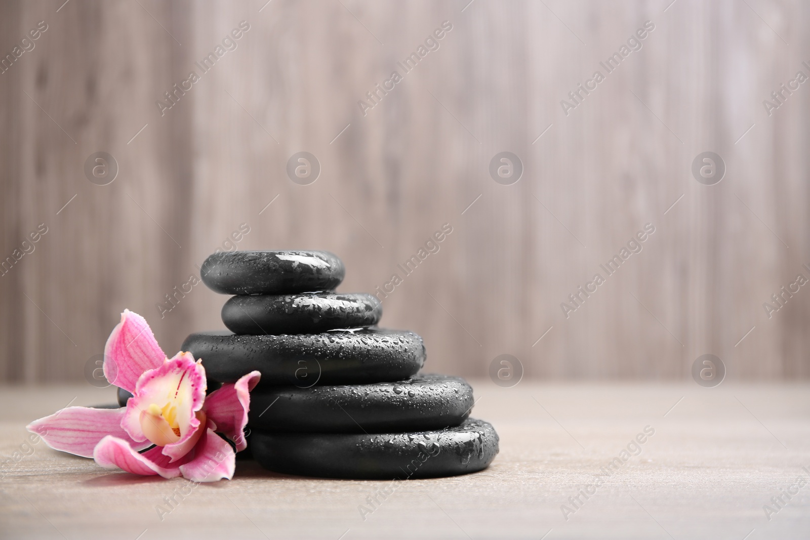 Photo of Stack of black spa stones with flower on wooden background. Space for text