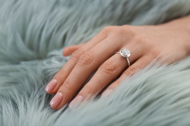 Young woman wearing beautiful engagement ring on faux fur rug, closeup