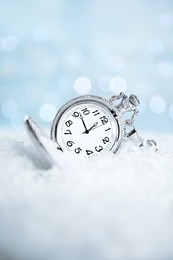 Photo of Pocket watch on snow against blurred lights. New Year countdown