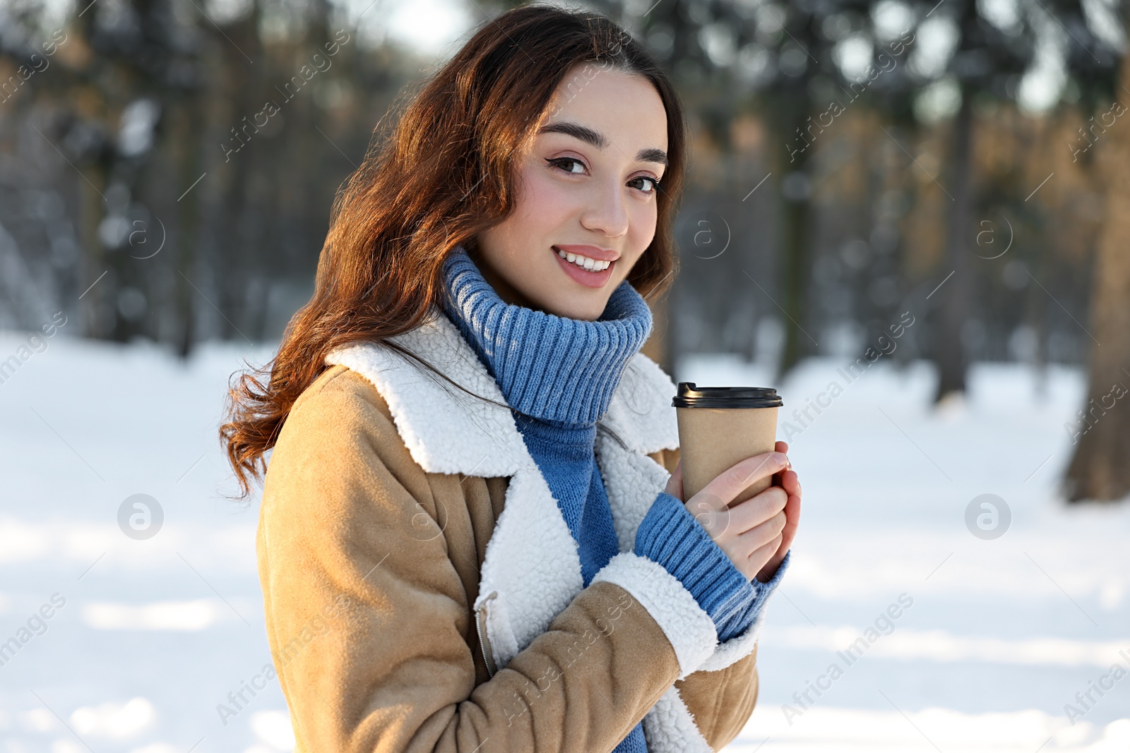 Photo of Portrait of smiling woman with paper cup of coffee in snowy park