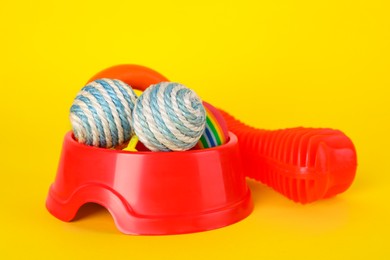 Photo of Various bright pet toys and bowl on yellow background