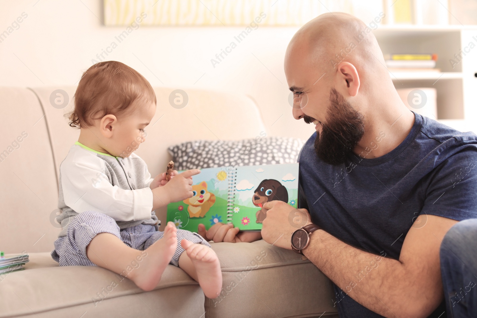 Photo of Dad reading book with his little son in living room