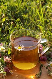 Photo of Cup of aromatic herbal tea and different wildflowers on green grass outdoors