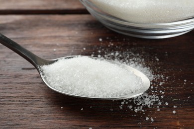 Photo of Spoon with granulated sugar on wooden table, closeup