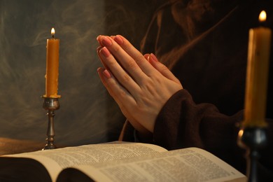 Photo of Woman praying at table with burning candles and Bible, closeup