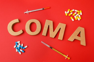 Photo of Word Coma of wooden letters, syringes and pills on red background, flat lay