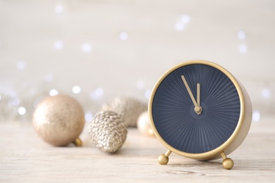 Stylish clock with decor on white wooden table against blurred Christmas lights, closeup. New Year countdown