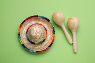 Photo of Colorful maracas and sombrero hat on light green background, flat lay. Musical instrument