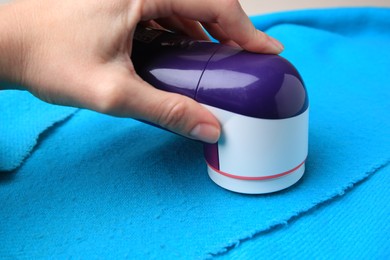 Photo of Woman using fabric shaver on light blue cloth with lint, closeup