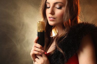 Beautiful young woman with microphone singing on color background with smoke, space for text