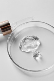 Petri dish with cosmetic serum and pipette on white background, closeup