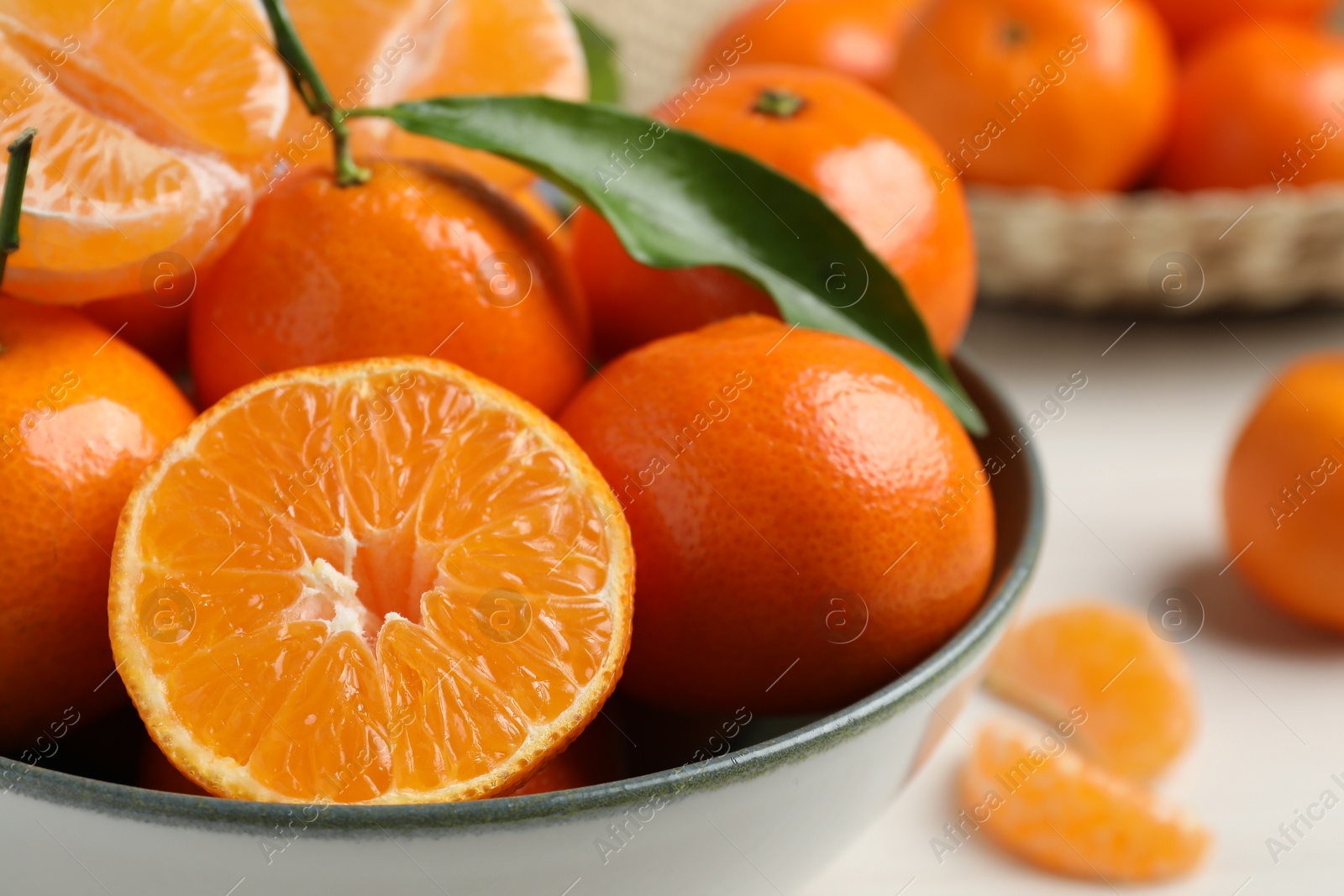 Photo of Delicious tangerines with green leaves in bowl on white wooden table, closeup