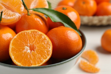 Photo of Delicious tangerines with green leaves in bowl on white wooden table, closeup