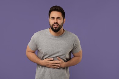 Young man suffering from stomach pain on purple background